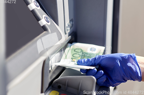 Image of hand in medical glove with money at atm machine