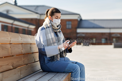 Image of woman in mask spraying hand sanitizer outdoors