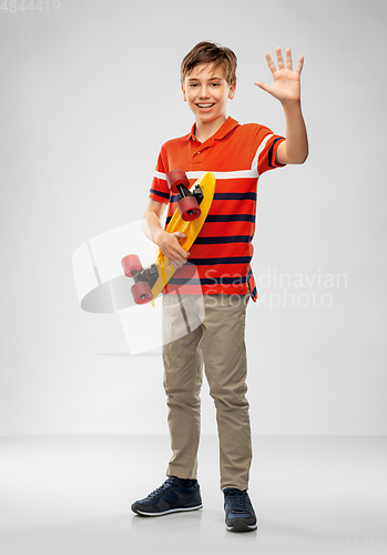 Image of smiling boy with short skateboard waving hand