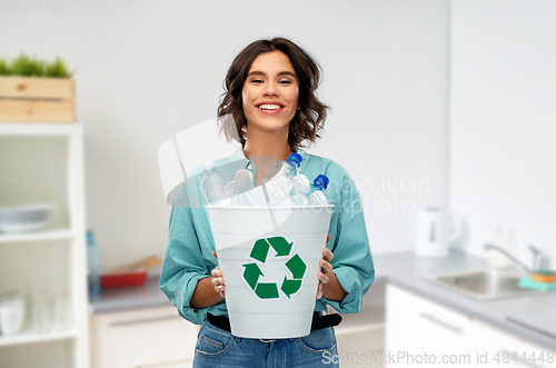 Image of smiling young woman sorting plastic waste at home