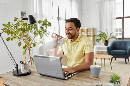 Image of man with laptop recording voice on phone at home