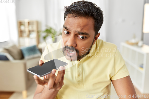 Image of angry man recording voice on smartphone at home