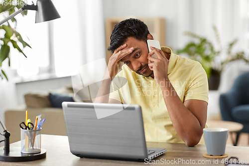 Image of indian man with laptop calling on phone at home