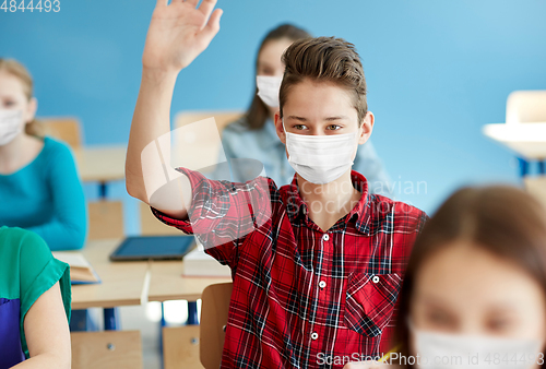 Image of student boy in mask with raised hand at school
