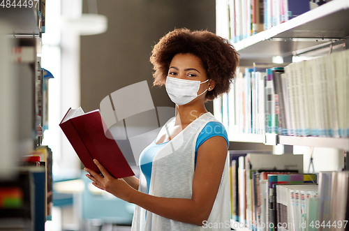 Image of african student girl in mask with book at library