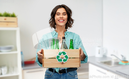Image of smiling young woman sorting glass waste at home