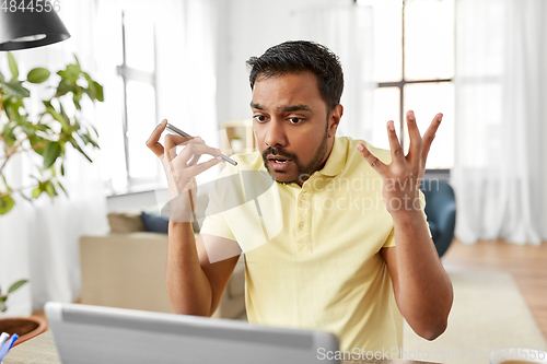 Image of man with laptop recording voice on phone at home