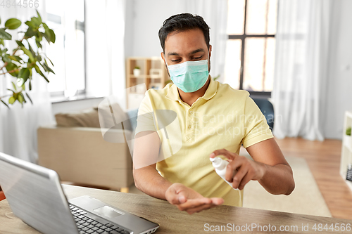 Image of man in mask using hand sanitizer at home office
