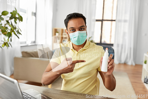 Image of man in mask showing hand sanitizer at home office