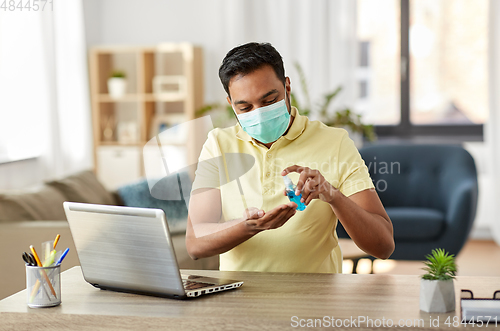 Image of man in mask using hand sanitizer at home office