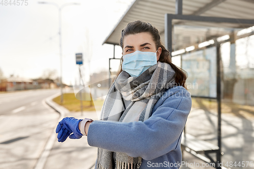 Image of woman in mask looking at wristwatch at bus stop