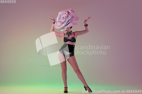 Image of Young female dancer with huge floral hats in neon light on gradient background