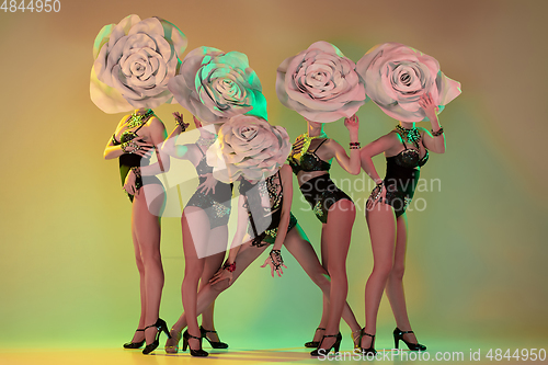 Image of Young female dancers with huge floral hats in neon light on gradient background