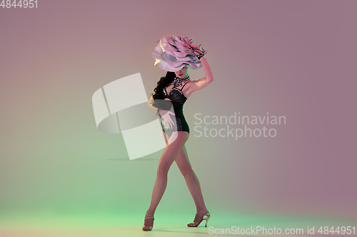 Image of Young female dancer with huge floral hats in neon light on gradient background