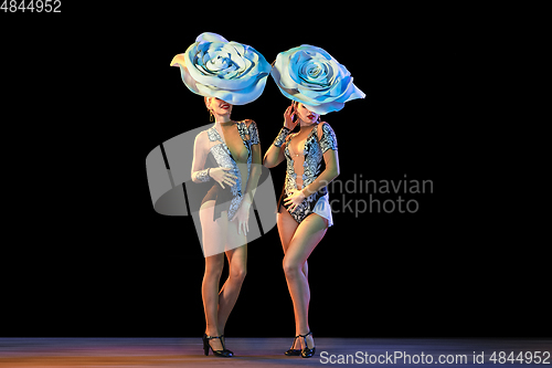 Image of Young female dancers with huge floral hats in neon light on black background