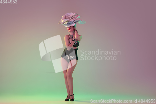 Image of Young female dancer with huge floral hats in neon light on gradient background