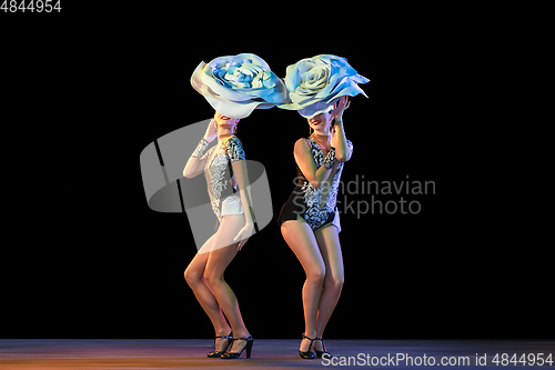 Image of Young female dancers with huge floral hats in neon light on black background