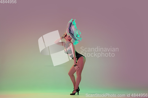 Image of Young female dancer with huge floral hats in neon light on gradient background