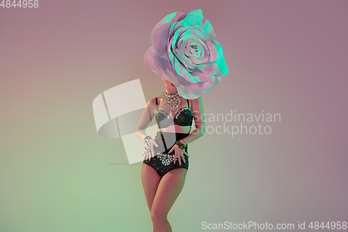 Image of Young female dancer with huge floral hats in neon light on gradient background