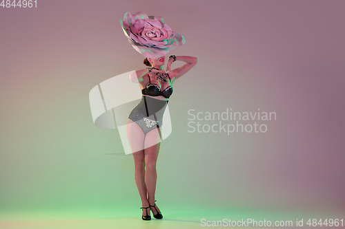 Image of Young female dancer with huge floral hats in neon light on gradient background