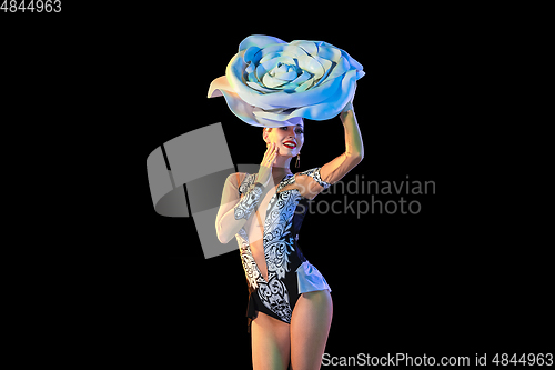 Image of Young female dancer with huge floral hat in neon light on black background