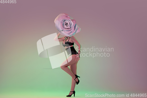 Image of Young female dancer with huge floral hats in neon light on gradient background