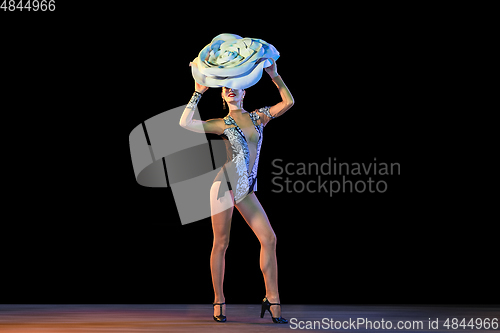Image of Young female dancer with huge floral hat in neon light on black background