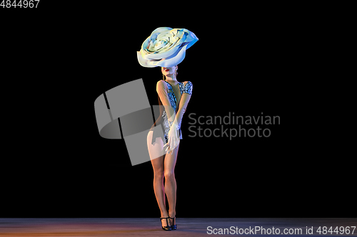 Image of Young female dancer with huge floral hat in neon light on black background