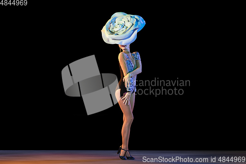 Image of Young female dancer with huge floral hat in neon light on black background