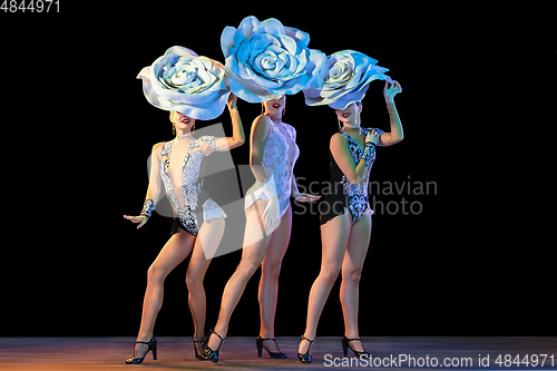 Image of Young female dancers with huge floral hats in neon light on black background