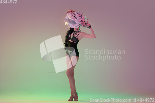 Image of Young female dancer with huge floral hats in neon light on gradient background