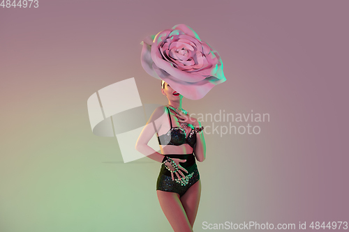 Image of Young female dancer with huge floral hats in neon light on gradient background