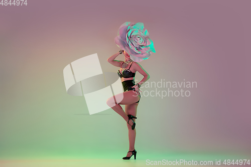 Image of Young female dancer with huge floral hats in neon light on gradient background