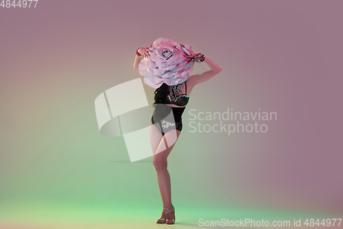 Image of Young female dancer with huge floral hats in neon light on gradient background