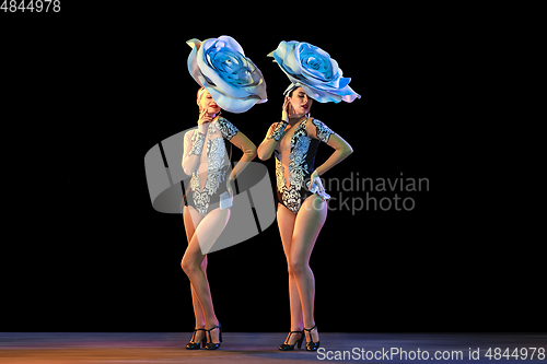 Image of Young female dancers with huge floral hats in neon light on black background