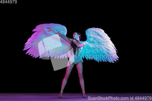 Image of Young female dancer with angel\'s wings in neon light on black background