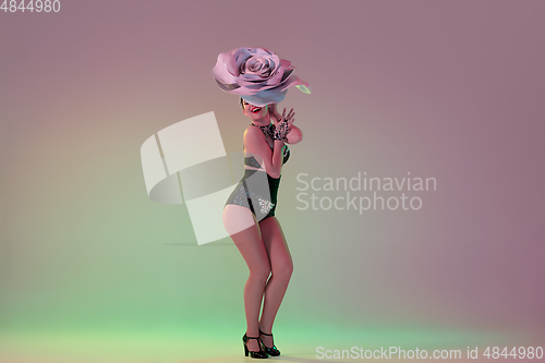 Image of Young female dancer with huge floral hats in neon light on gradient background