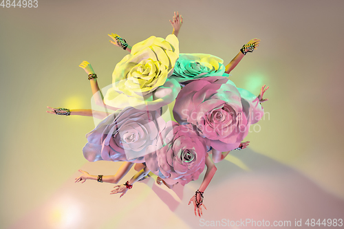 Image of Young female dancers with huge floral hats in neon light on gradient background