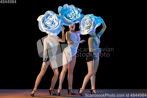 Image of Young female dancers with huge floral hats in neon light on black background