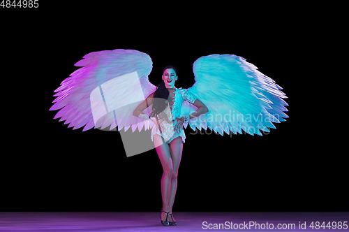 Image of Young female dancer with angel\'s wings in neon light on black background