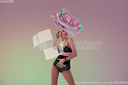 Image of Young female dancer with huge floral hats in neon light on gradient background