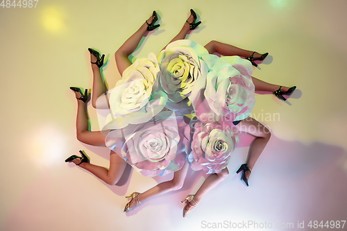 Image of Young female dancers with huge floral hats in neon light on gradient background