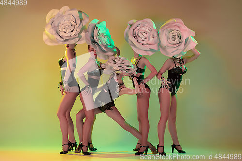 Image of Young female dancers with huge floral hats in neon light on gradient background