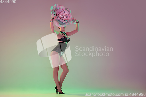 Image of Young female dancer with huge floral hats in neon light on gradient background