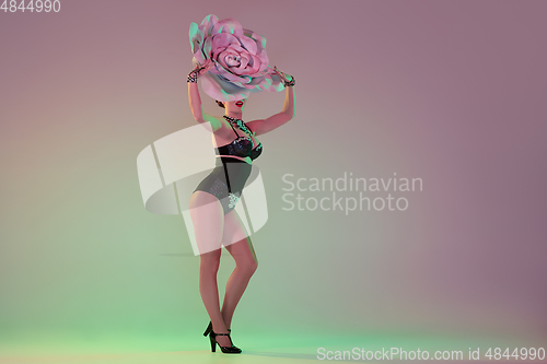 Image of Young female dancer with huge floral hats in neon light on gradient background