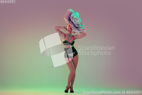 Image of Young female dancer with huge floral hats in neon light on gradient background