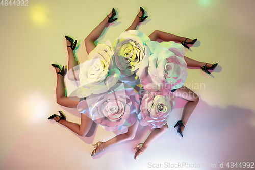 Image of Young female dancers with huge floral hats in neon light on gradient background