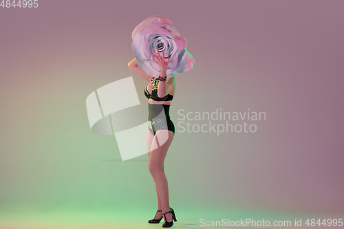 Image of Young female dancer with huge floral hats in neon light on gradient background