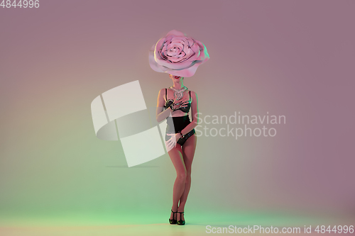 Image of Young female dancer with huge floral hats in neon light on gradient background