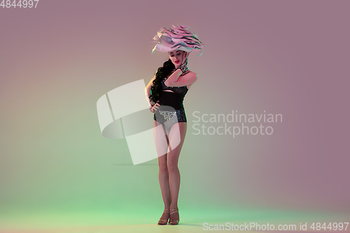 Image of Young female dancer with huge floral hats in neon light on gradient background